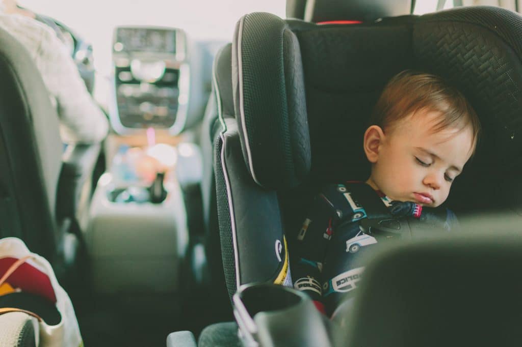 A baby boy sleeping in the back seat of the car in a rear facing car seat.